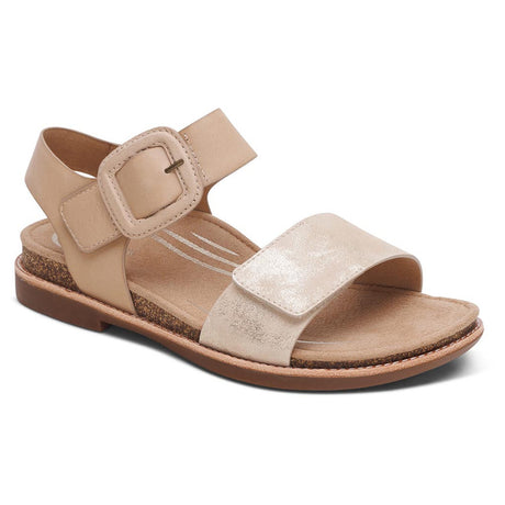 Women’s champagne gold sandal with a large buckle ankle strap, shimmering front strap, and cork-detailed sole. Style #FC173