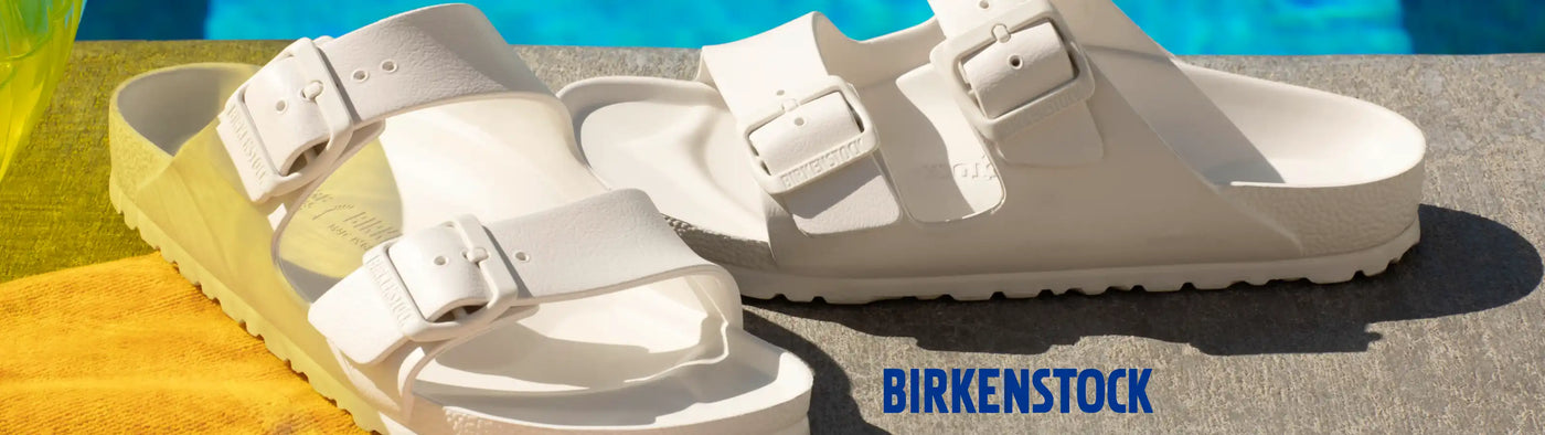 White Birkenstock sandals on a textured surface with a blurred pool background