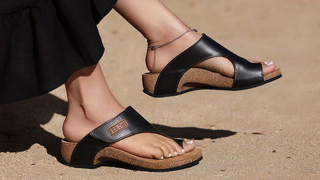 Black sandals with cork soles worn on a sandy surface